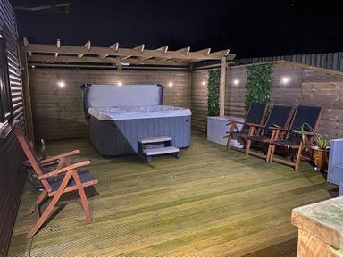 An outdoor wooden deck with a hot tub under a pergola and several wooden chairs at Willow Retallack in Retallack near St Columb Major