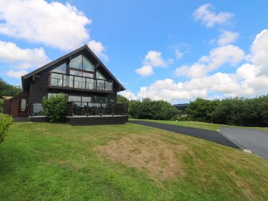 A two story wooden house with balconies and glass railings on a lawn with a driveway at Willow Retallack in Retallack near St Columb Major