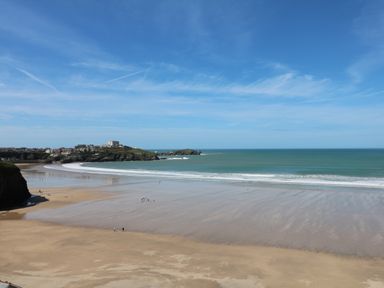 A beach with waves and people on the sand near a coastal town and hills