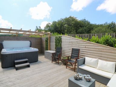 An outdoor deck with a hot tub chairs and sofa with cushions at Willow Retallack in Retallack near St Columb Major