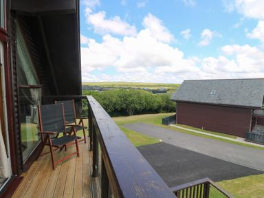 A balcony with two chairs overlooking a driveway and a building with sloped roof at Willow Retallack in Retallack near St Columb Major