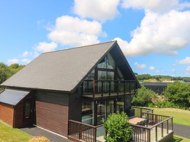A two story wooden house with a balcony and outdoor dining area surrounded by grass at Willow, Retallack in Retallack near St Columb Major