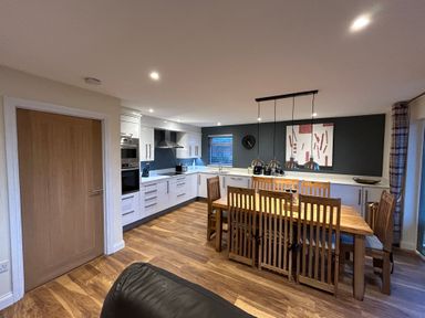 A kitchen with white cabinets a wooden dining table and chairs and pendant lights at Willow Retallack in Retallack near St Columb Major