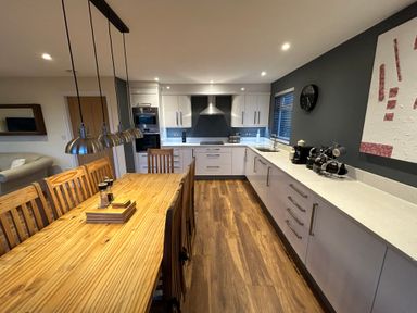 A kitchen with a wooden dining table and chairs next to white cabinets with appliances at Willow Retallack in Retallack near St Columb Major