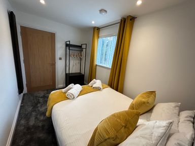 A bedroom with a bed with rolled towels on it a clothes rack with hangers a window with yellow curtains and a wooden door at Willow Retallack Retallack near St Columb Major