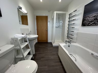 A bathroom with a toilet, sink, white shelving unit, bathtub, shower, and wooden door at Willow, Retallack in Retallack near St Columb Major