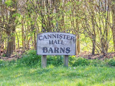 A wooden sign reading Cannister Hall Barns on grass with trees in the background