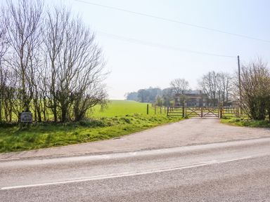 A country road leading to a gated entrance with fields and a house in the background at The Dairy Barn in Toftrees near Fakenham