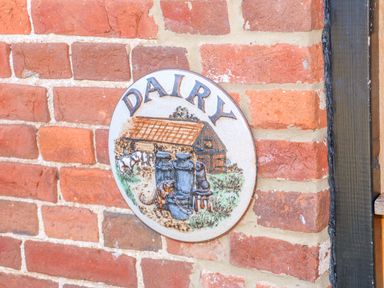 A brick wall with a round ceramic plaque showing a dairy scene at The Dairy Barn in Toftrees near Fakenham
