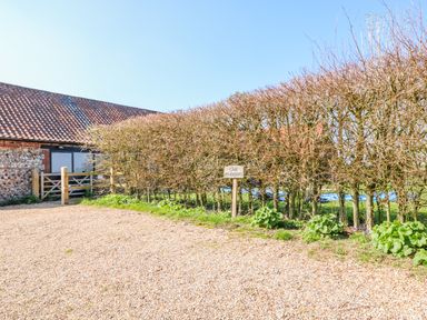 A gravel driveway with a wooden gate and a car parking sign next to a hedge at The Dairy Barn in Toftrees near Fakenham