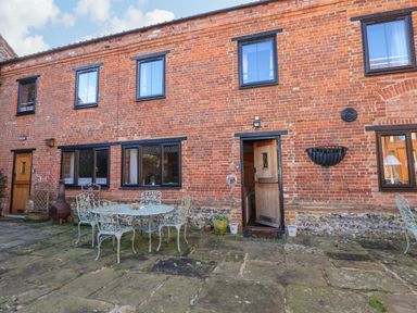 A brick building with multiple windows and doors a patio area with metal table and chairs at The Dairy Barn in Toftrees near Fakenham