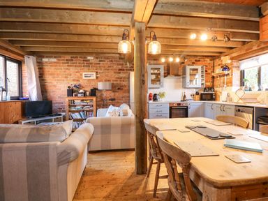 A kitchen and living area with wooden beams a dining table couches and a bookshelf at The Dairy Barn in Toftrees near Fakenham