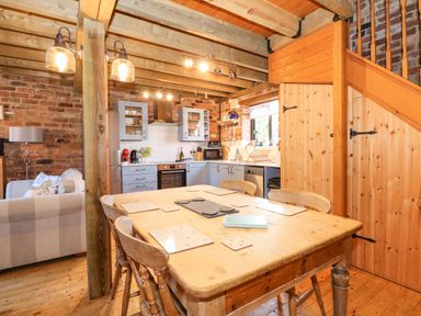 A kitchen and dining area with wooden table and chairs next to wooden stairs and brick walls at The Dairy Barn in Toftrees near Fakenham