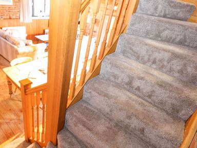 Carpeted staircase with wooden banister overlooking a living room with table and sofa at The Dairy Barn in Toftrees near Fakenham