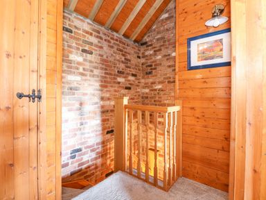 A stair landing with wooden walls a framed picture a light fixture and exposed brick at The Dairy Barn in Toftrees near Fakenham