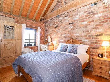 A bedroom with a wooden bed with blue bedding two nightstands a dresser a wardrobe a chair and a window at The Dairy Barn in Toftrees near Fakenham