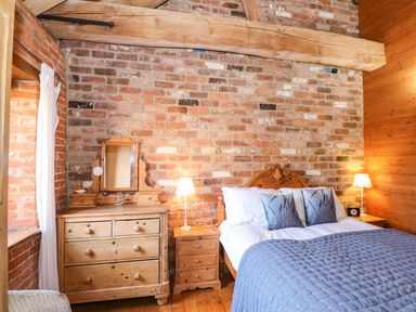 A bedroom with a wooden bed blue bedding wooden dresser and nightstand with lamps at The Dairy Barn in Toftrees near Fakenham