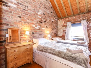 A bedroom with two single beds a wooden dresser with a mirror and lamps on a brick wall at The Dairy Barn in Toftrees near Fakenham