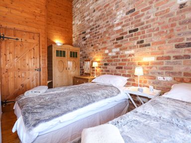 A bedroom with two single beds bedside lamps a wooden wardrobe and a brick wall at The Dairy Barn in Toftrees near Fakenham