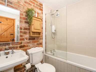 A bathroom with a sink toilet shower bathtub and wooden cabinet on a brick wall at The Dairy Barn in Toftrees near Fakenham
