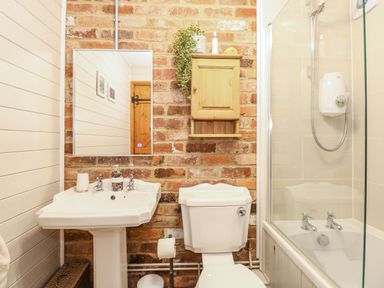 A bathroom with a sink toilet shower and a wooden cabinet on a brick wall at The Dairy Barn in Toftrees near Fakenham