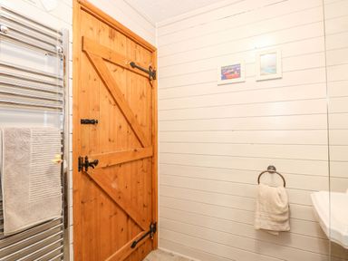 A bathroom with a wooden door white paneled walls a towel hanging on a ring and another towel on a heated towel rail at The Dairy Barn in Toftrees near Fakenham