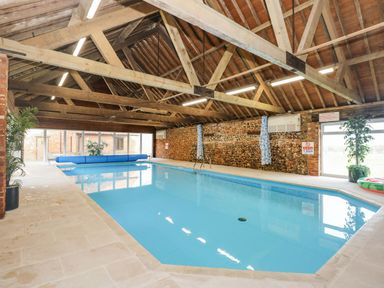 An indoor swimming pool with stone walls wooden ceiling beams and large windows at The Dairy Barn in Toftrees near Fakenham