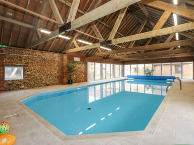 An indoor swimming pool with stone walls and wooden ceiling beams at The Dairy Barn in Toftrees near Fakenham