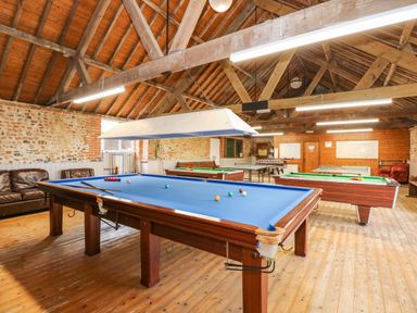 A game room with multiple billiard tables leather sofas foosball table and wooden beams at The Dairy Barn in Toftrees near Fakenham