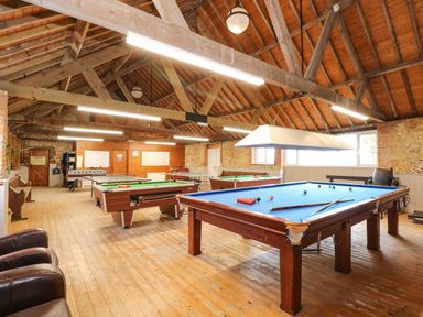 A game room with pool tables and a foosball table under wooden beams at The Dairy Barn in Toftrees near Fakenham