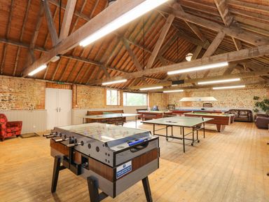 A game room with foosball tables table tennis tables pool tables and seating at The Dairy Barn in Toftrees near Fakenham