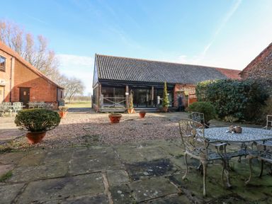 An outdoor patio area with metal table and chairs potted plants and buildings surrounding the courtyard at The Dairy Barn in Toftrees near Fakenham