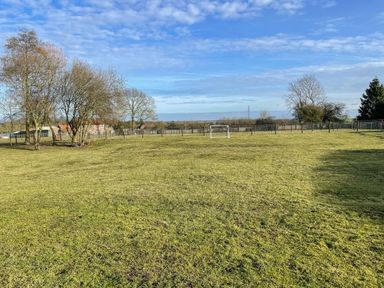 A field with short grass and a small soccer goal surrounded by fences and trees at The Dairy Barn in Toftrees near Fakenham