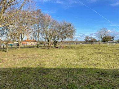 A grassy fenced garden with trees and a small goalpost near a brick house at The Dairy Barn in Toftrees near Fakenham