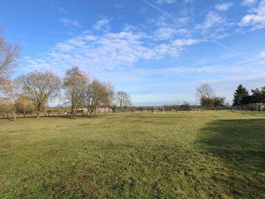 A large grassy field with a small soccer goal and trees under a blue sky at The Dairy Barn in Toftrees near Fakenham