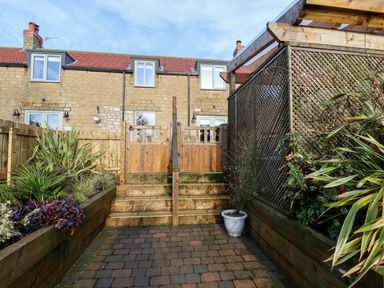 A backyard garden with wooden fencing plants and stone steps leading to a two story stone house at Tawny Cottage in Irton Moor near Scarborough