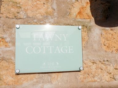 A glass sign on a stone wall with text Tawny Cottage at Riggs Head Farm country cottages