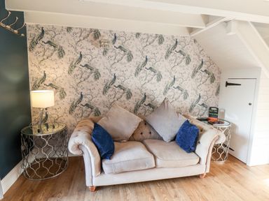 A beige sofa with cushions between two round metal side tables with a lamp and small chalkboard under slanted ceiling at Tawny Cottage Irton Moor near Scarborough