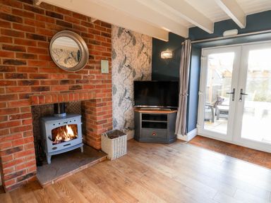 A living room with a wood-burning stove in a brick fireplace and a television on a stand near glass doors at Tawny Cottage in Irton Moor near Scarborough