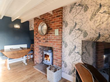 A room with a brick fireplace and stove a wooden table and chairs and a television on a stand at Tawny Cottage in Irton Moor near Scarborough