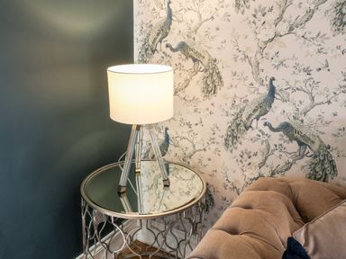 A side table with a lamp next to a sofa and wallpaper with peacock designs at Tawny Cottage in Irton Moor near Scarborough