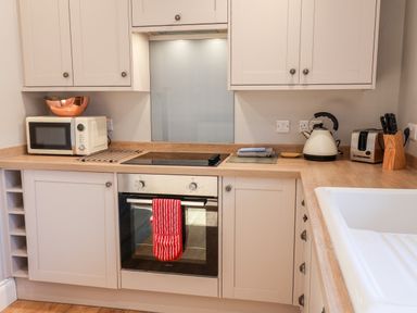 A kitchen countertop with a microwave a kettle a toaster a knife block and an oven with a red oven mitt at Tawny Cottage in Irton Moor near Scarborough