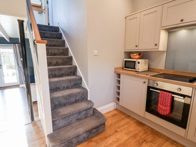 A carpeted staircase next to a kitchen with wooden floor cabinets a microwave and an oven with a red oven mitt at Tawny Cottage Irton Moor near Scarborough