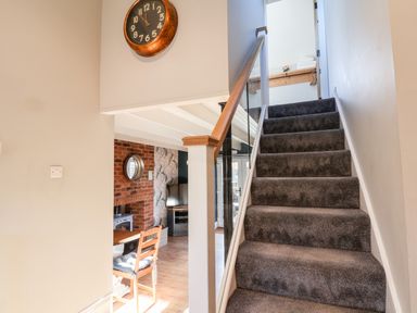 A staircase with carpet leading upstairs next to a wall clock and a dining area with a chair and table at Tawny Cottage in Irton Moor near Scarborough