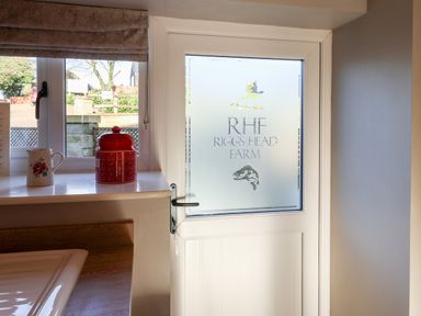 A kitchen door with frosted glass and a window with a red jar and a floral jug on the windowsill at Tawny Cottage in Irton Moor near Scarborough