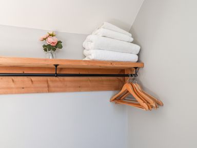 A wooden shelf with folded white towels a small vase with pink flowers and wooden hangers on a metal rod at Tawny Cottage in Irton Moor near Scarborough