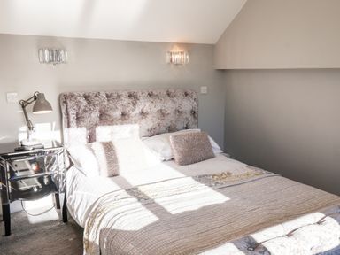 A bedroom with a bed with a tufted headboard two bedside lamps and a side table at Tawny Cottage in Irton Moor near Scarborough