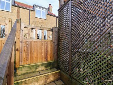 Wooden gate and steps leading to stone house with windows and lattice fence at Tawny Cottage in Irton Moor near Scarborough