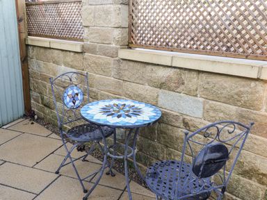 A small outdoor seating area with a round mosaic table and two metal chairs on a paved patio at Tawny Cottage in Irton Moor near Scarborough