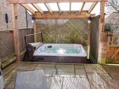 An outdoor hot tub under a wooden pergola with lattice fencing on a stone patio at Tawny Cottage in Irton Moor near Scarborough